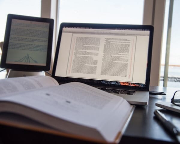 Laptop and tablet displaying documents, open book nearby.