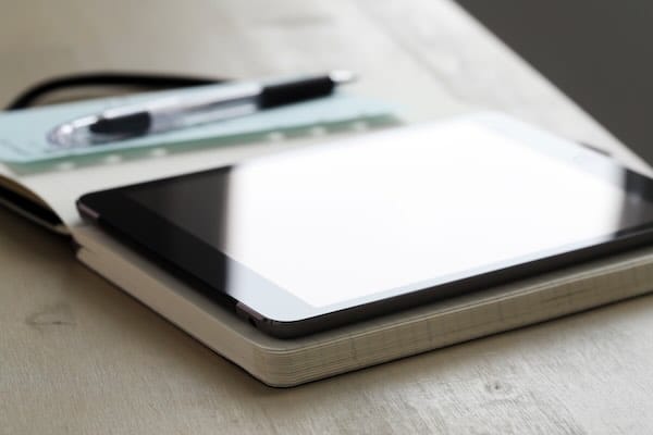 Tablet on notebook with pen beside it.
