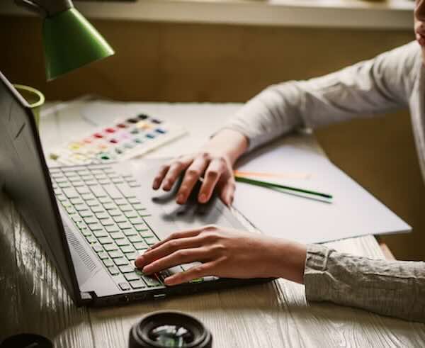 Person working on a laptop beside watercolor paints.